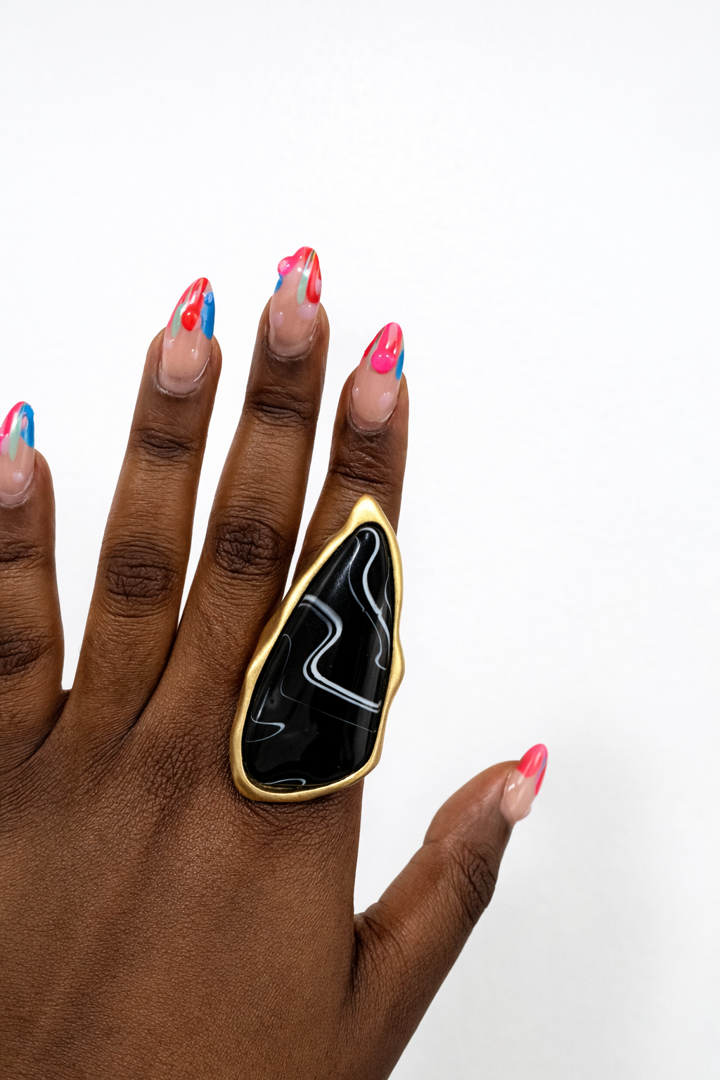Hand wearing a black and gold ring with colorful nail polish on a white background