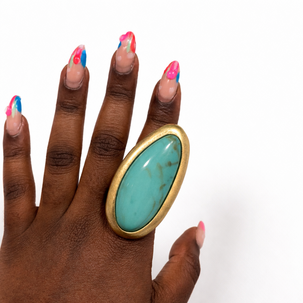 Hand wearing a large turquoise ring with gold band on a white background