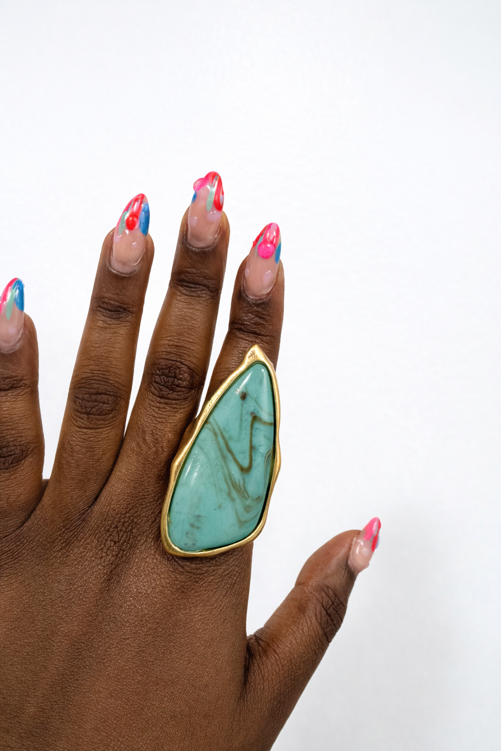 Hand wearing a turquoise ring with gold band on a white background