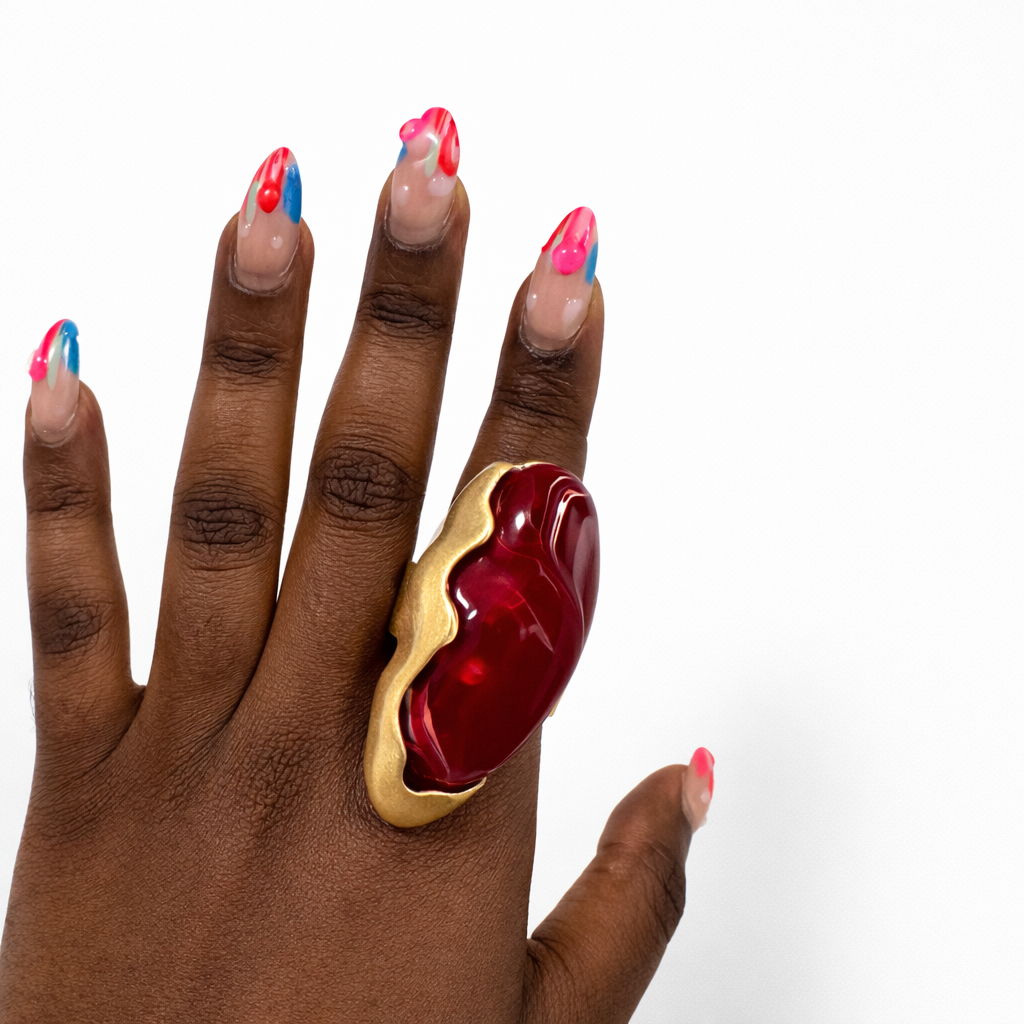 Hand wearing a large red and gold ring on a white background